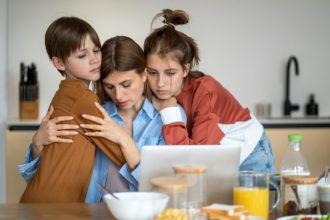 Children embracing and supporting tired single mother at home