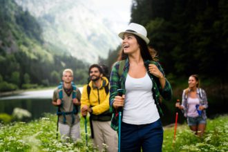 Group of smiling friends hiking with backpacks outdoors. Travel, tourism, hike and people concept